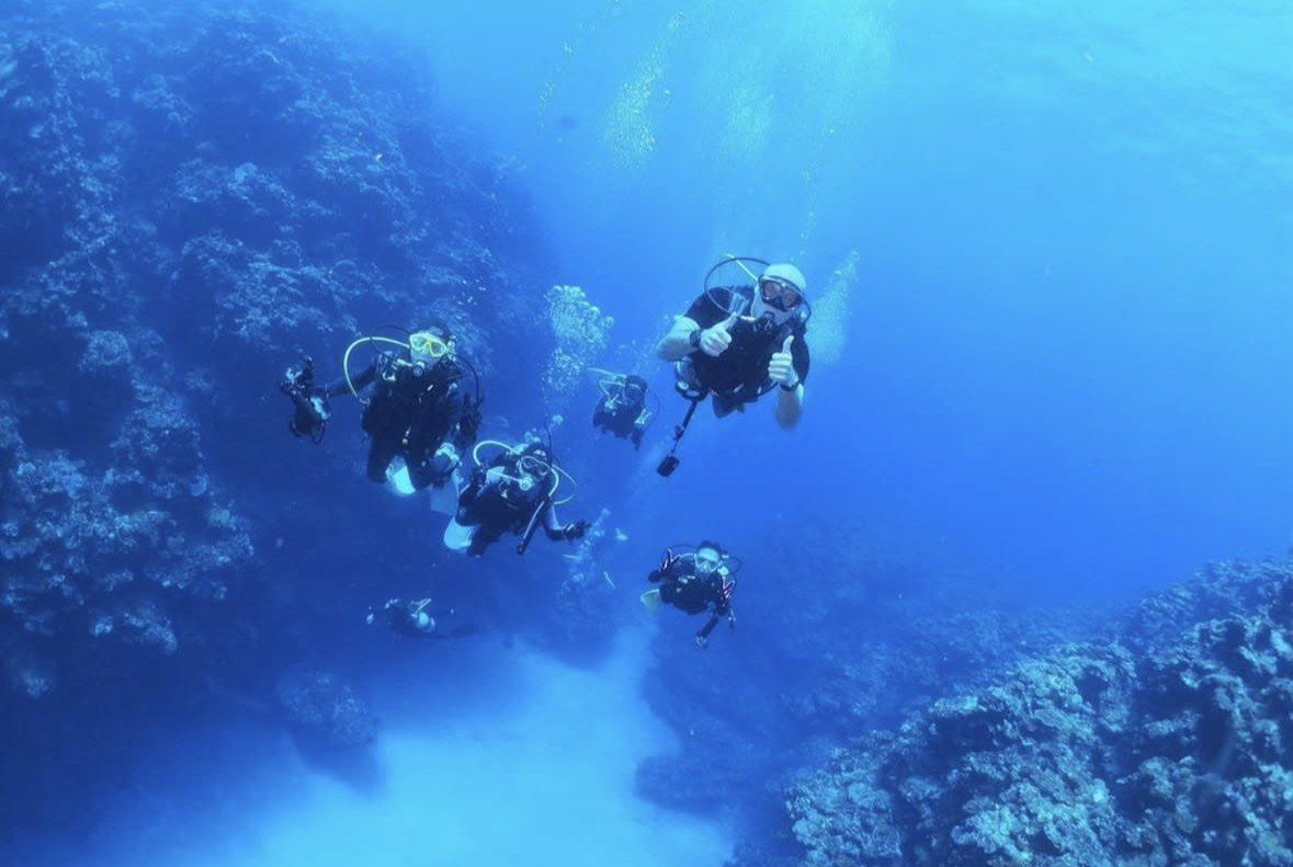 Group of scuba divers along a coral wall in clear Kona water
