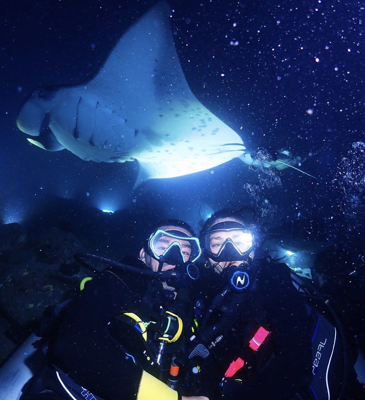 Two scuba divers at night as a manta glides overhead, Kona